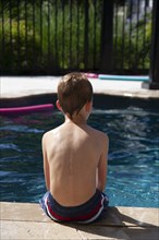 Rear view of young boy sitting at edge of pool