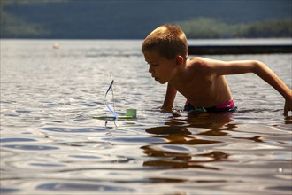 Young boy with homemade toy sailboat in lake
