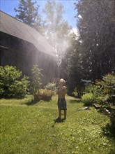 Young boy playing with sprinkler hose in yard