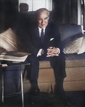 Man in suit with hands clasped sitting on sofa