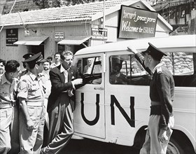 Danny Kaye leaning against UN vehicle near sign saying "Welcome to Israel"