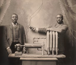 American inventor Charles S.L. Baker (right), standing behind heating radiator, system, Martin W.