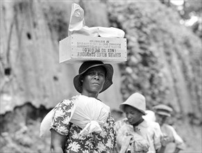 Woman transporting packages  of surplus  relief commodities, a New Deal government program, on her