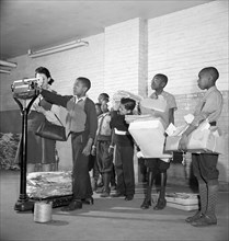 Students lined up to weigh collected scrap paper at school during Scrap Salvage Campaign, Victory