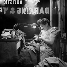 Jewish woman darning clothes in window of darning and weaving shop, Broome Street, New York City,