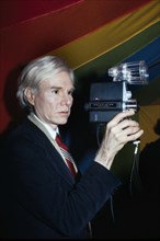 American pop artist Andy Warhol, half-length portrait holding Polaroid Polavision camera, Bernard