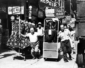 Men pulling racks of clothing on busy sidewalk in Garment District, New York City, New York, USA,