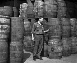 Stanley Hyams, co-owner of Washington Pickle Works, holding two pickles in a room full of barrels