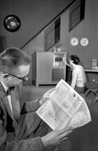 Man reading newspaper while woman is turning radio dial in living room, Warren K. Leffler, U.S.