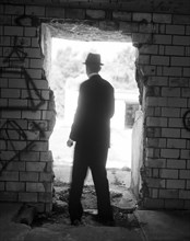 Rear view of mid-adult man in suit and hat standing in open doorway