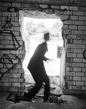 Blurred rear view of mid-adult man in suit and hat slightly crouching in open doorway