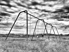 Swing set in field with long grass and dramatic sky