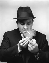 Mid-adult man in suit and hat lighting a cigarette