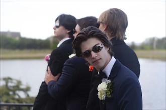 Young boy in sunglasses and suit facing camera with three friends, also in suits, in background