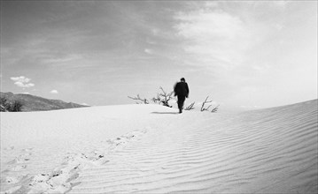 Rear view of mid-adult man in suit running up a sand dune