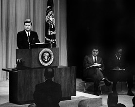 U.S. President John F. Kennedy at lectern during press conference, Press Secretary Pierre Salinger