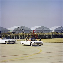 U.S. President John Kennedy riding in open convertible car past soldiers in review formation while