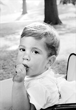 John Kennedy, Jr., sucking his finger while sitting in carriage on South Lawn, Washington, D.C.,