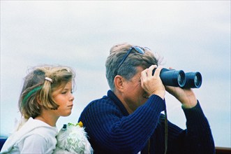 U.S. President John F. Kennedy looking through binoculars while sitting next to his daughter,