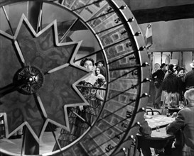 Yvonne De Carlo (viewed through wheel spokes), on-set of the western film, "Border River",