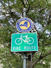 Signs for Bike Route and Empire State Trail against leafy green tree, New York City, New York, USA