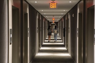 Rear view of two people walking down hotel hallway, diminishing perspective