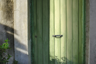 Old green wood door with center black metal handle in shadow