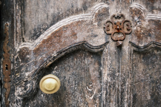 Weathered wood door with intricate carvings, rusted metal hardware and gold-colored door knob