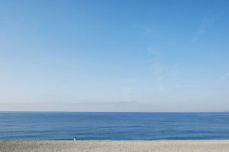 Rear view of solitary woman sitting on beach and looking out to sea