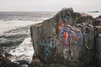 Large rock covered in colorful graffiti along  coast