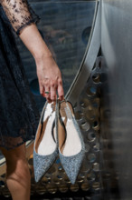 Two sparkling silver shoes dangling from woman's fingertips