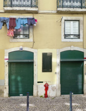 Clothes hanging on line on building facade above two shuttered green doors, Lisbon, Portugal