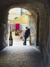 Rear view of a man standing at the end of an alley near an outdoor café, Sarlat-la-Canéda,