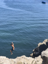 High angle view of teen boy jumping off cliff into sea, Cascais, Portugal