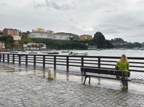 Rear view of woman sitting on bench looking at boats in harbor, Mugardos, Galicia, Spain