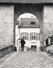 Man walking along cobblestone street in rain, Cluny, France