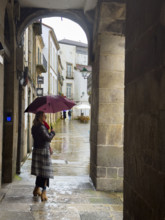 Woman with umbrella in village square on rainy day, Santiago de Compostela, Galicia, Spain