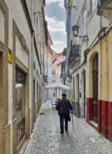 Rear view of man walking down narrow street, Coimbra, Portugal