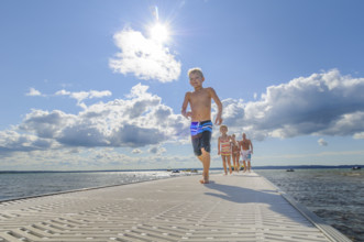 Parents with young children walking along lakeside dock on summer day