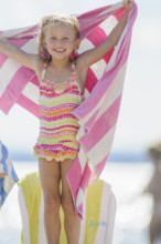 Smiling young girl holding up towel with pink stripes at beach