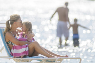 Mother kissing young daughter on forehead in foreground, father wading into water with son in