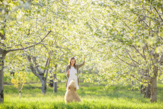 Young adult woman and her dog enjoying blossoming cherry orchard