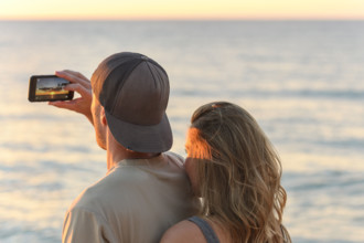 Young adult couple taking photo of sunset at Lake Michigan, Traverse City, Michigan, USA