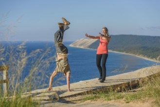 Young adult man performing handstand while young adult woman watches with arms extended forward