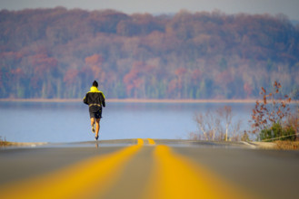 Rear view of mid-adult man running toward lake in autumn