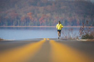 Mid-adult man running with lake and autumn scenery in background