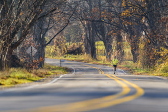 Mid-adult man running along scenic road in autumn