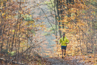 Mid-adult man running along scenic wooded path in autumn