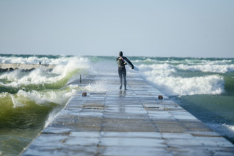 Rear view of surfer in wetsuit walking to end of pier