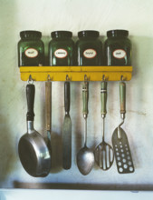 Kitchen utensils hanging below a spice rack with mint, caraway, thyme, and sage jars, Arthur S.